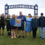 Harborfest officials and sponsors celebrate the new venue at Cahill Pier. In front, holding the official 2024 Harborfest poster: Maria and Dave Johnson, owners of C's Farm Market, sponsors of the Cahill Pier Stage. Back row, left to right: Dan Harrington, Harborfest Executive Director; Jessica Westberry of Breitbeck Park sponsor Novelis; Angela Cleary of Cahill Pier Stage music sponsor Community Bank; Kylie Wyman of Fireworks Spectacular sponsor Pathfinder Bank; Maria Hudson of sponsor Constellation Energy; Chuck Handley, Harborfest board president; and Carol Dillabough, Harborfest Marketing and Membership Coordinator.